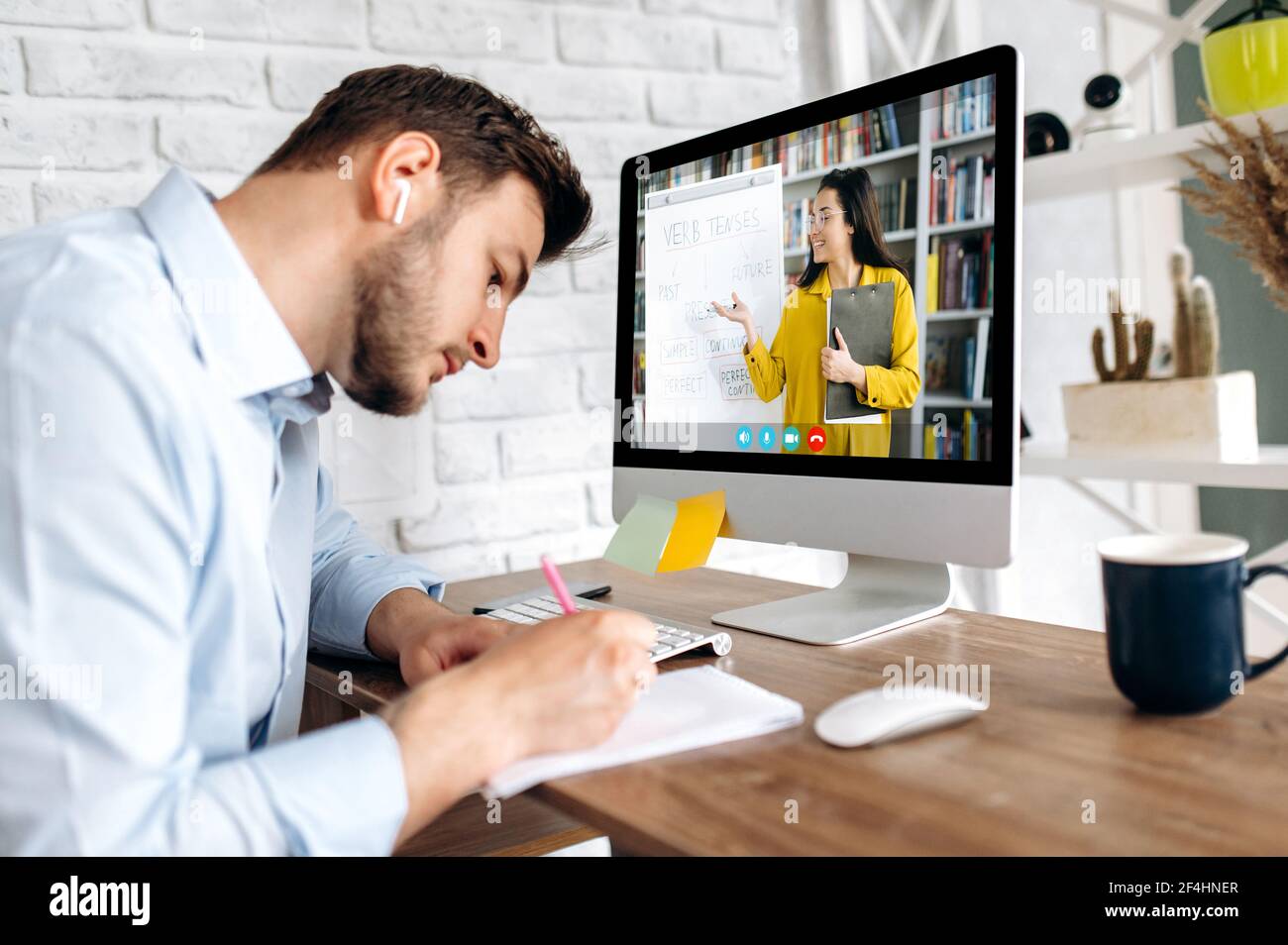 Online-Bildung, E-Learning. Junger Mann, Fernstudium per Videoanruf, Notizen machen, auf dem Computer-Bildschirm führt der Lehrer eine Online-Lektion zeigt Informationen auf einem Flipchart,Lernen von zu Hause Stockfoto