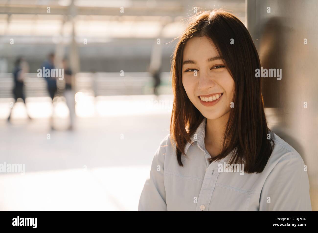 Portrait des schönen asiatischen jungen Unternehmers, der sich an der Säule lehnt Vor dem Büro, während Sie lächeln und die Kamera betrachten Stockfoto