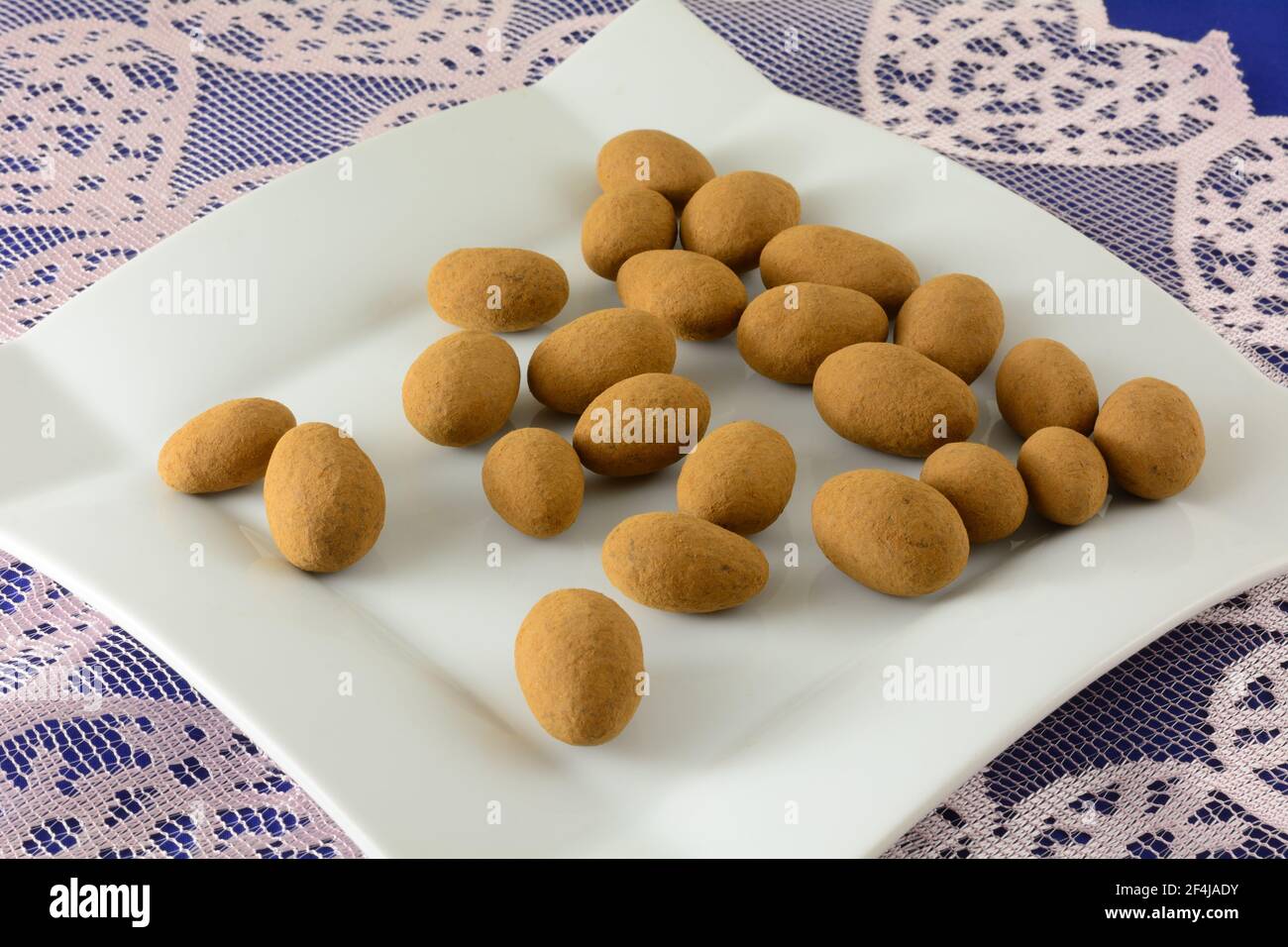 Kakaostaubte Mandeln Snack auf weißem Dessertteller auf Spitze Tischläufer Stockfoto