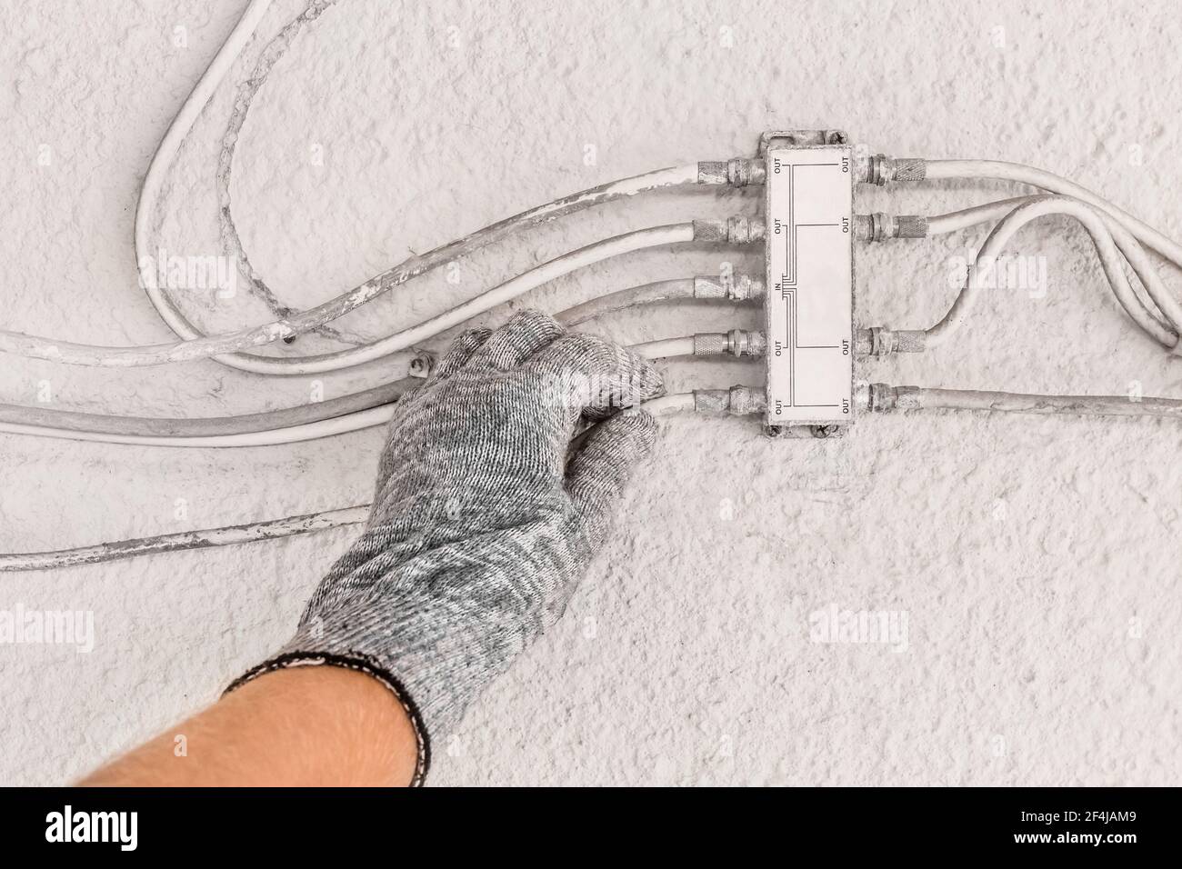 Hand des Industriearbeiters im Bauhandschuh überprüft Antennensplitter auf weißem Wandhintergrund. Stockfoto