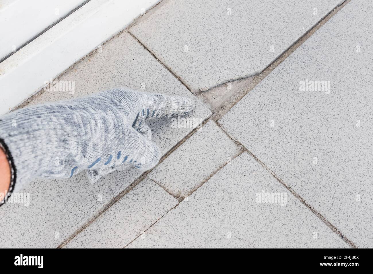 Hand des Industriearbeiters in der Konstruktion Handschuhtpunkte auf beschädigtem grauem Fliesenhintergrund. Renovierungskonzept. Stockfoto