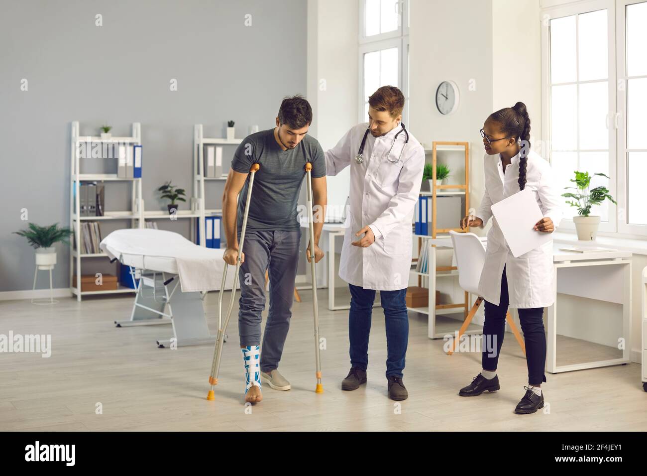 Ein Team von Ärzten verschiedener Nationalitäten im Krankenhaus hilft ihrem Patienten mit gebrochenem Knöchel. Stockfoto