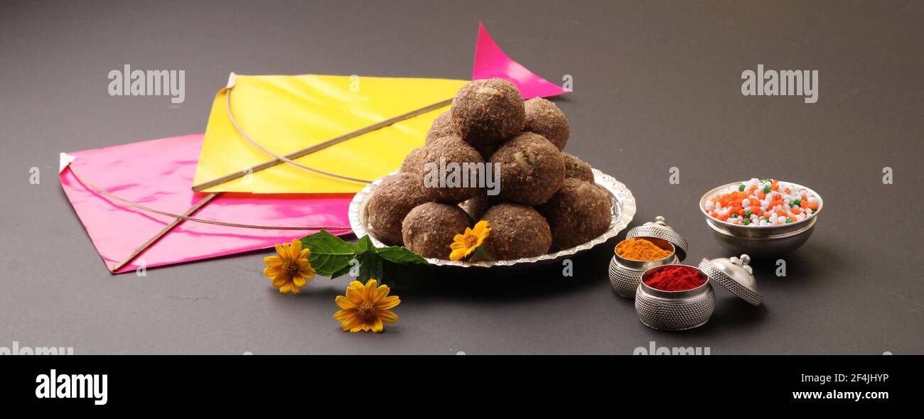 Til Gul ODER Sweet Sesam Laddu mit Drachenmodell, haldi Kumkum und Zuckerkristallen für das Makar Sankranti Festival auf schwarzem Hintergrund. Stockfoto