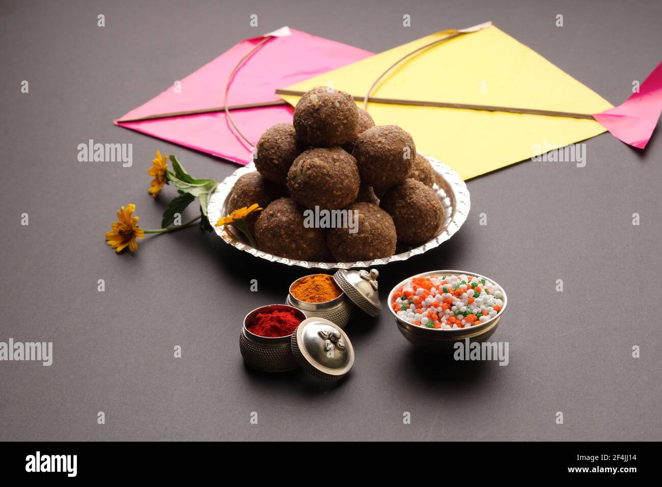 Til Gul ODER Sweet Sesam Laddu mit Drachenmodell, haldi Kumkum und Zuckerkristallen für das Makar Sankranti Festival auf schwarzem Hintergrund. Stockfoto