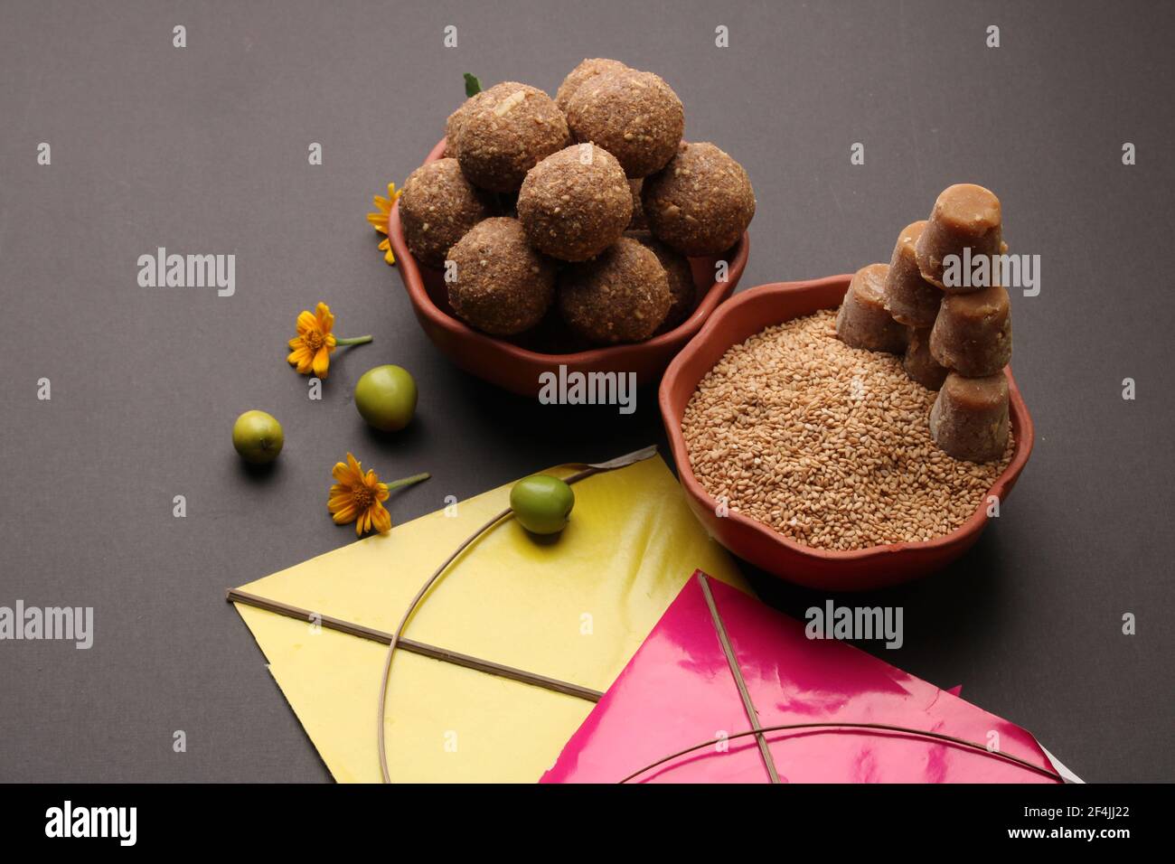 Til Gul ODER Sweet Sesam Laddu mit Drachenmodell, haldi Kumkum und Zuckerkristallen für das Makar Sankranti Festival auf schwarzem Hintergrund. Stockfoto