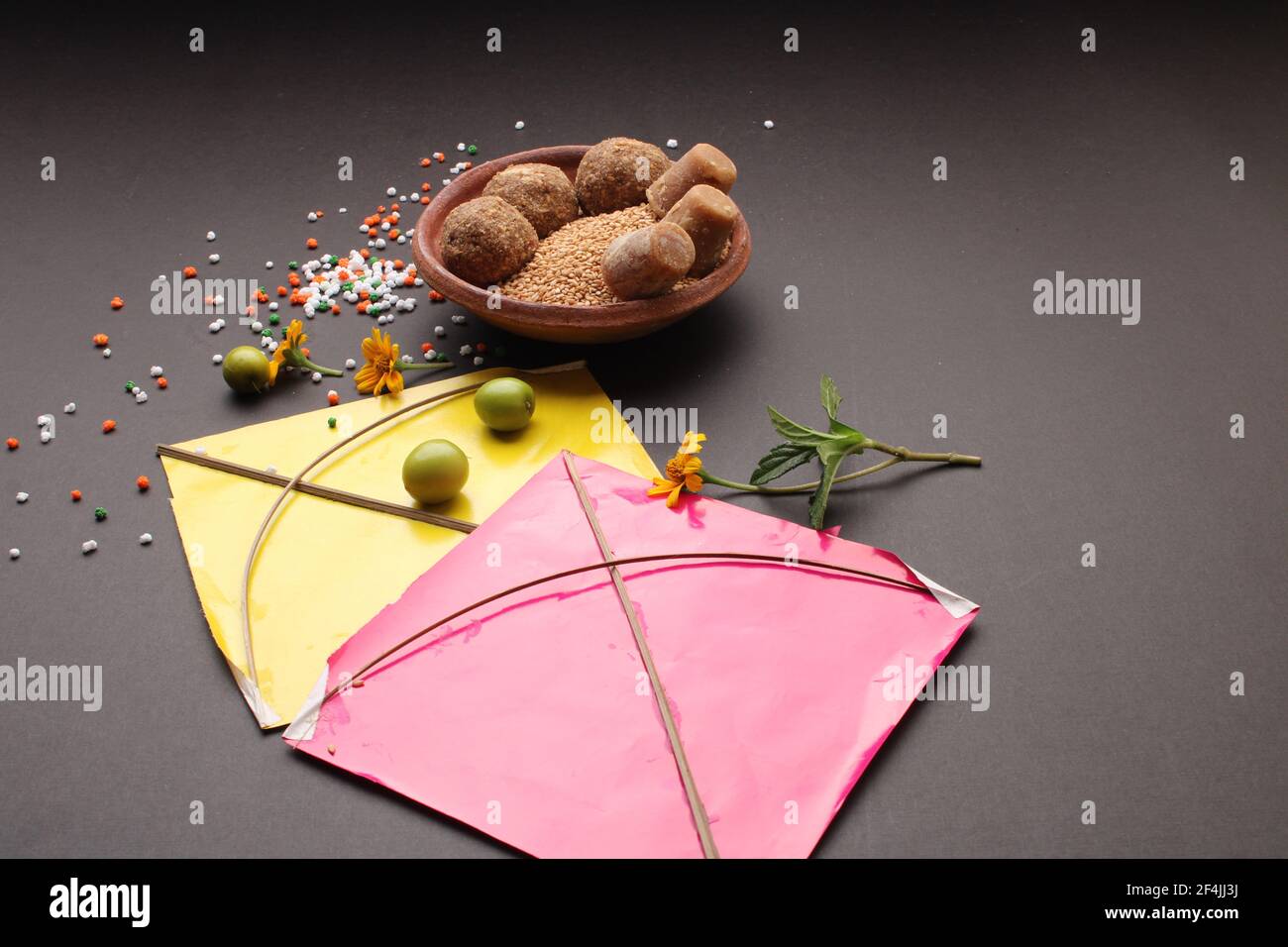 Til Gul ODER Sweet Sesam Laddu mit Drachenmodell, haldi Kumkum und Zuckerkristallen für das Makar Sankranti Festival auf schwarzem Hintergrund. Stockfoto