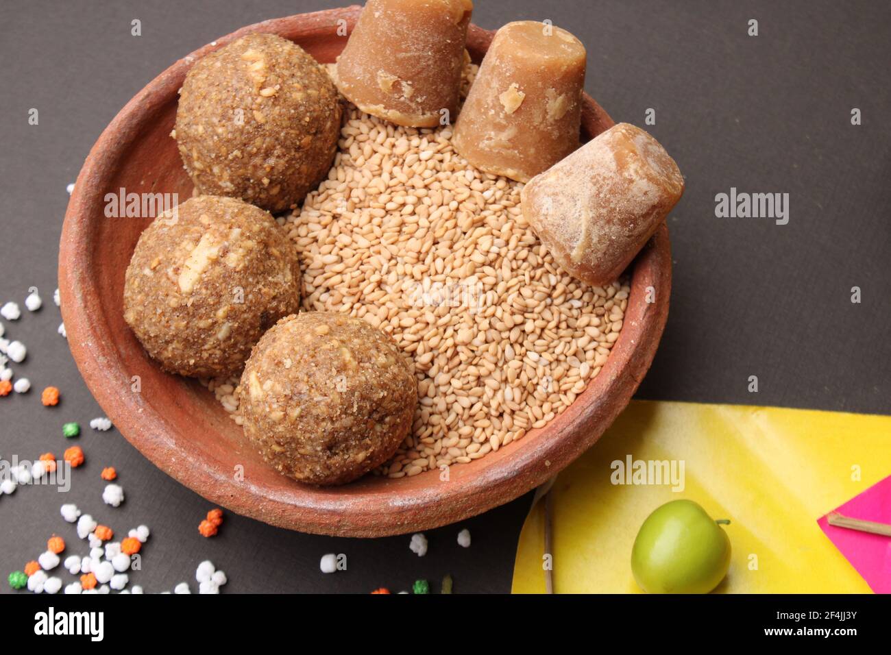 Til Gul ODER Sweet Sesam Laddu mit Drachenmodell, haldi Kumkum und Zuckerkristallen für das Makar Sankranti Festival auf schwarzem Hintergrund. Stockfoto