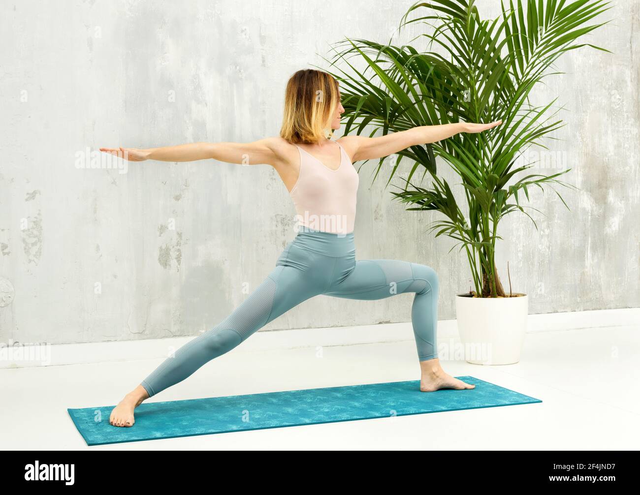 Frau, die eine Virabhadrasana II vorwärts Ausfallschritt Yoga Pose tut, um ihre Oberschenkel-, Hüftbeuge- und Leistenmuskeln in einer Gesundheit und Fitness zu dehnen und zu stärken Stockfoto