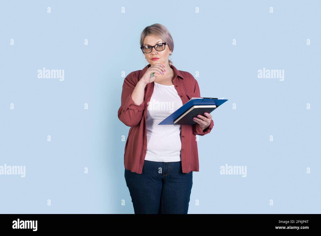 Ältere kaukasische Geschäftsfrau posiert auf einer blauen Studiowand Einige Ordner halten und eine Brille tragen, die auf die Kamera schaut Stockfoto
