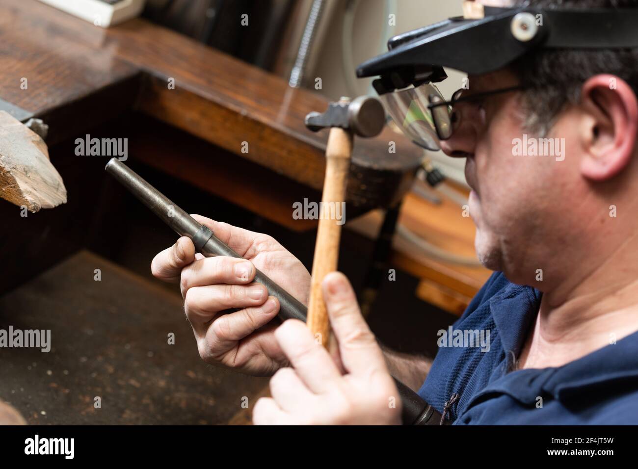 Ein Goldschmied hält einen Silberring und formt ihn mit einer Form und einem Hammer. Stockfoto