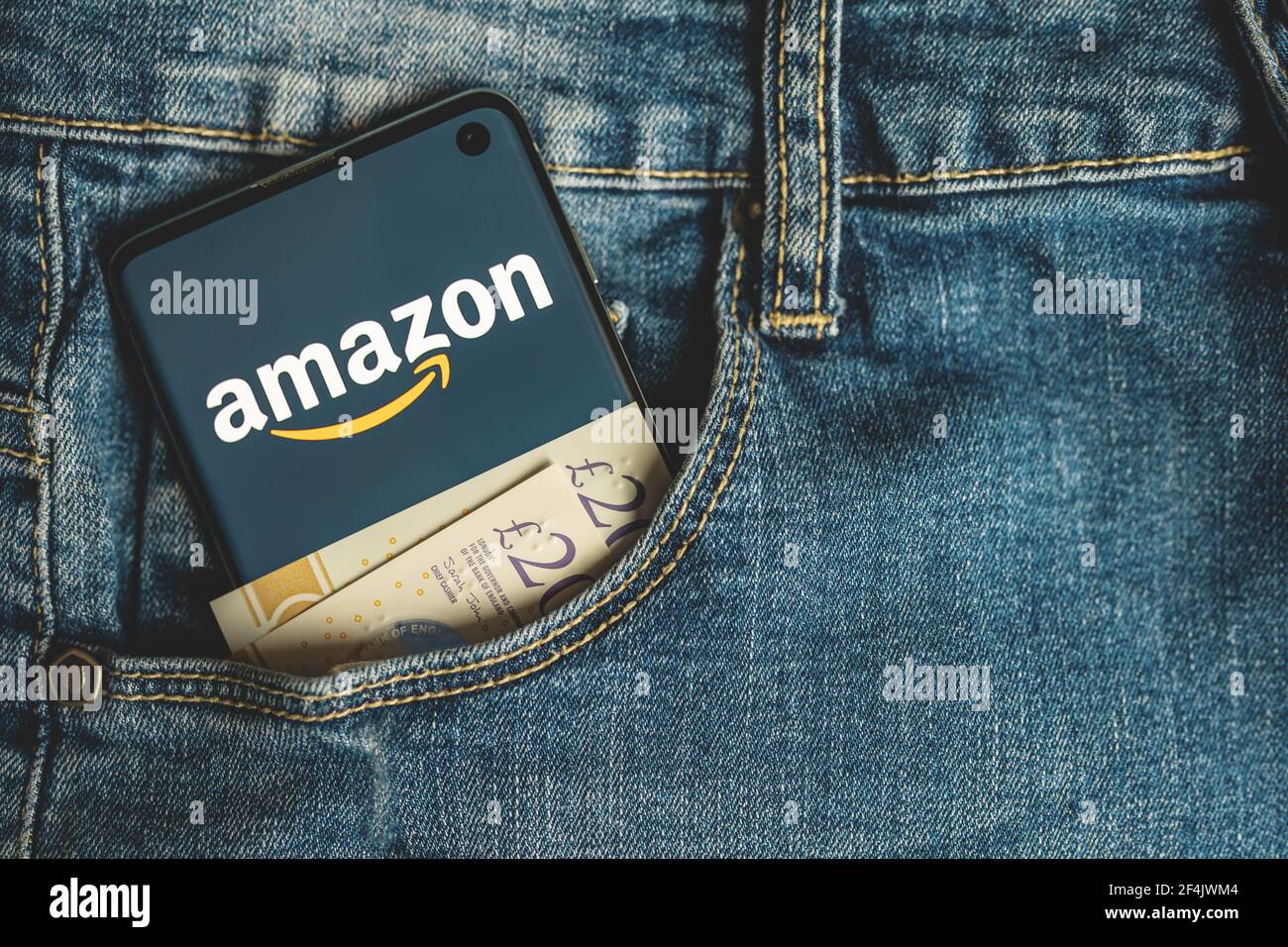 Smartphone mit Amazon App-Logo mit britischen Pfund Bargeld in Blaue Jeans-Tasche Stockfoto