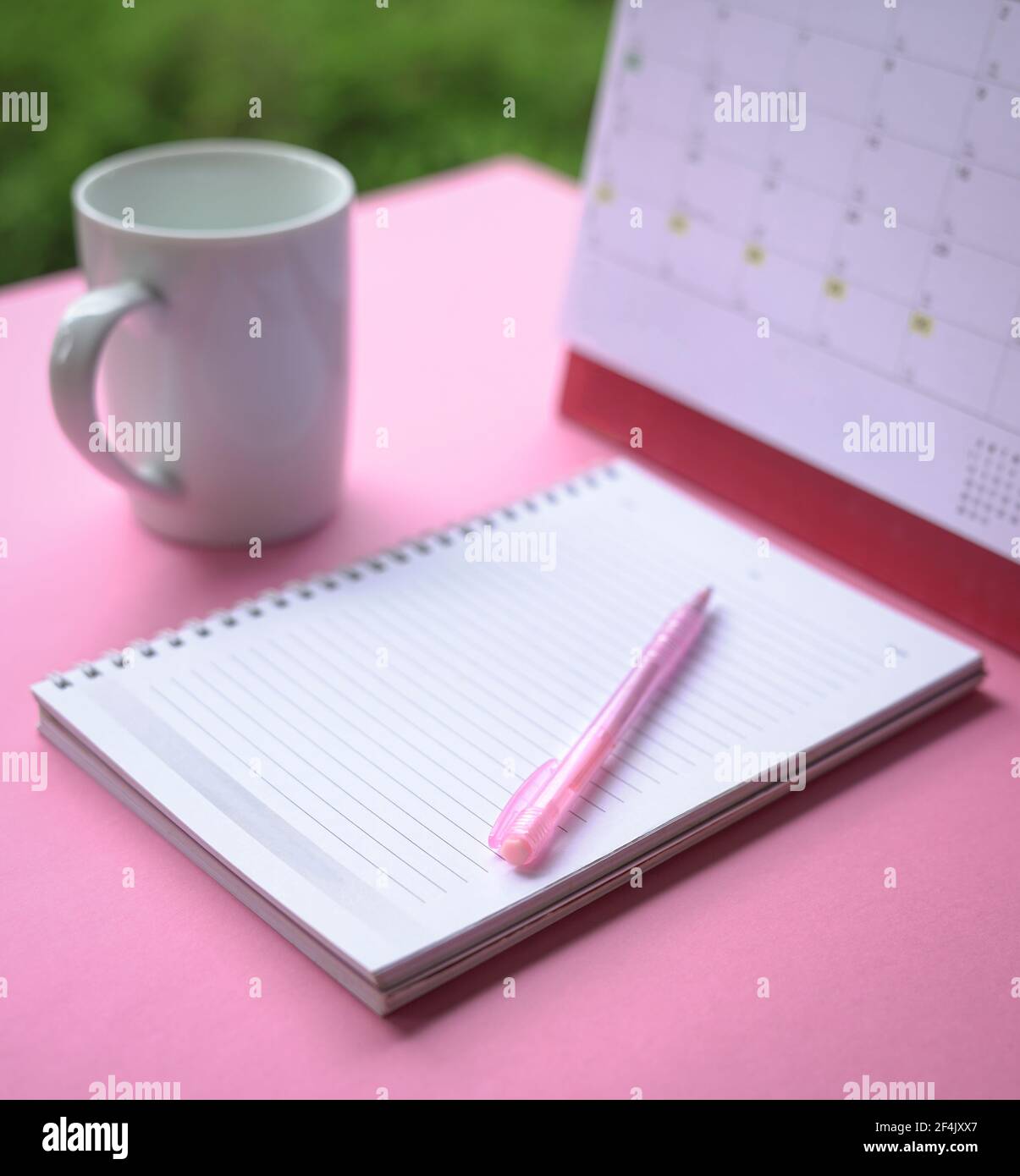 Pinker Stift auf dem Notizbuch mit Kalender und Tasse Kaffee im Hintergrund. Selektiver Fokus. Stockfoto