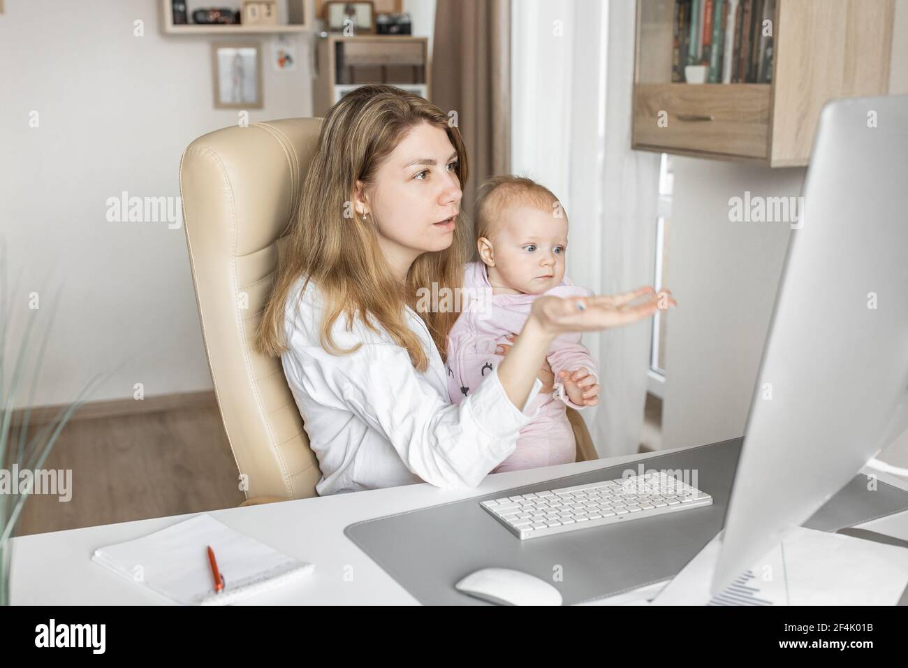 Erfolgreiche Geschäftsfrau Remote zu Hause arbeiten, während Babysitting kleine Tochter. Schöne junge Mutter mit kleinem Kind in den Armen Diskus Arbeit Stockfoto