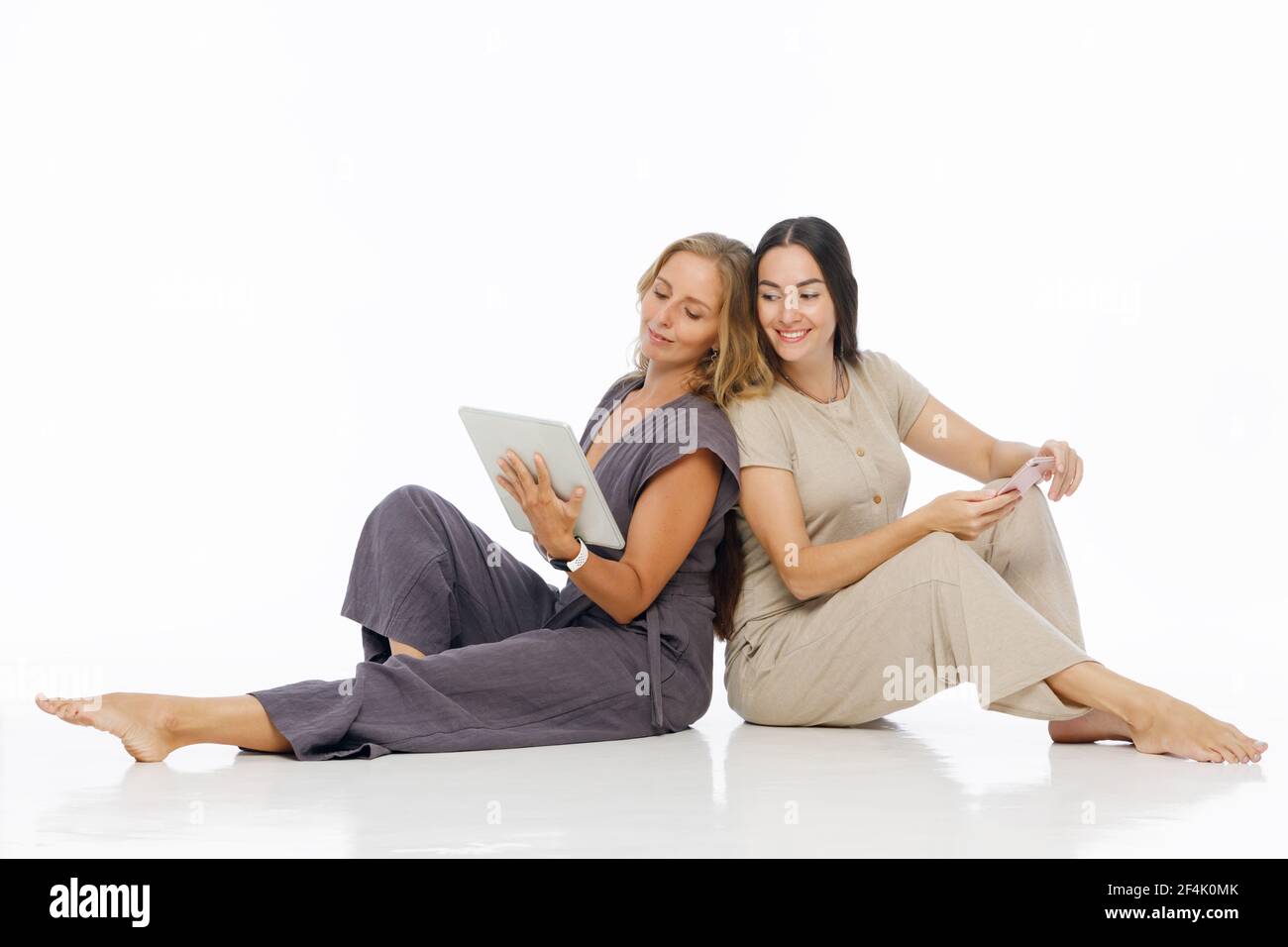 Junge attraktive Frauen sitzen auf dem Boden, arbeiten an Tablet-Computer und Smartphone. Zwei Bloggermädchen schreiben den Text auf Internet-Blog. Teamarbeit und Probel Stockfoto