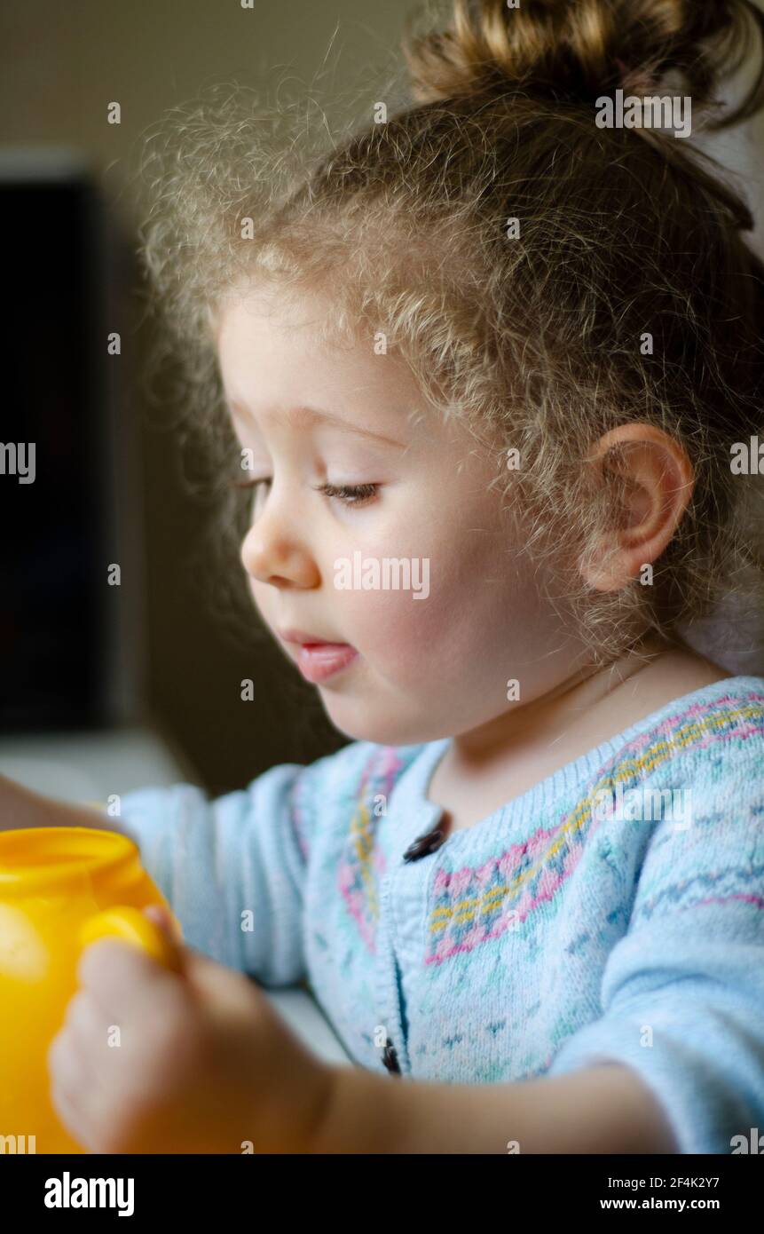 Mollige kleine Mädchen mit flatternden blonden Haaren spielt mit ihrem Spielzeug. Selektive Fokus Wange und Gesicht Stockfoto