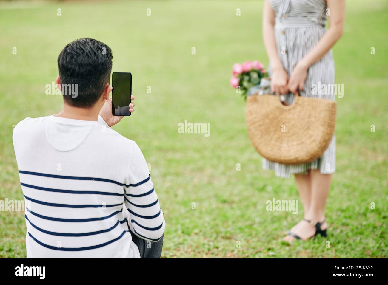 Junger Mann fotografiert seine Freundin mit Weidensack Von rosa Rosen im Stadtpark Stockfoto