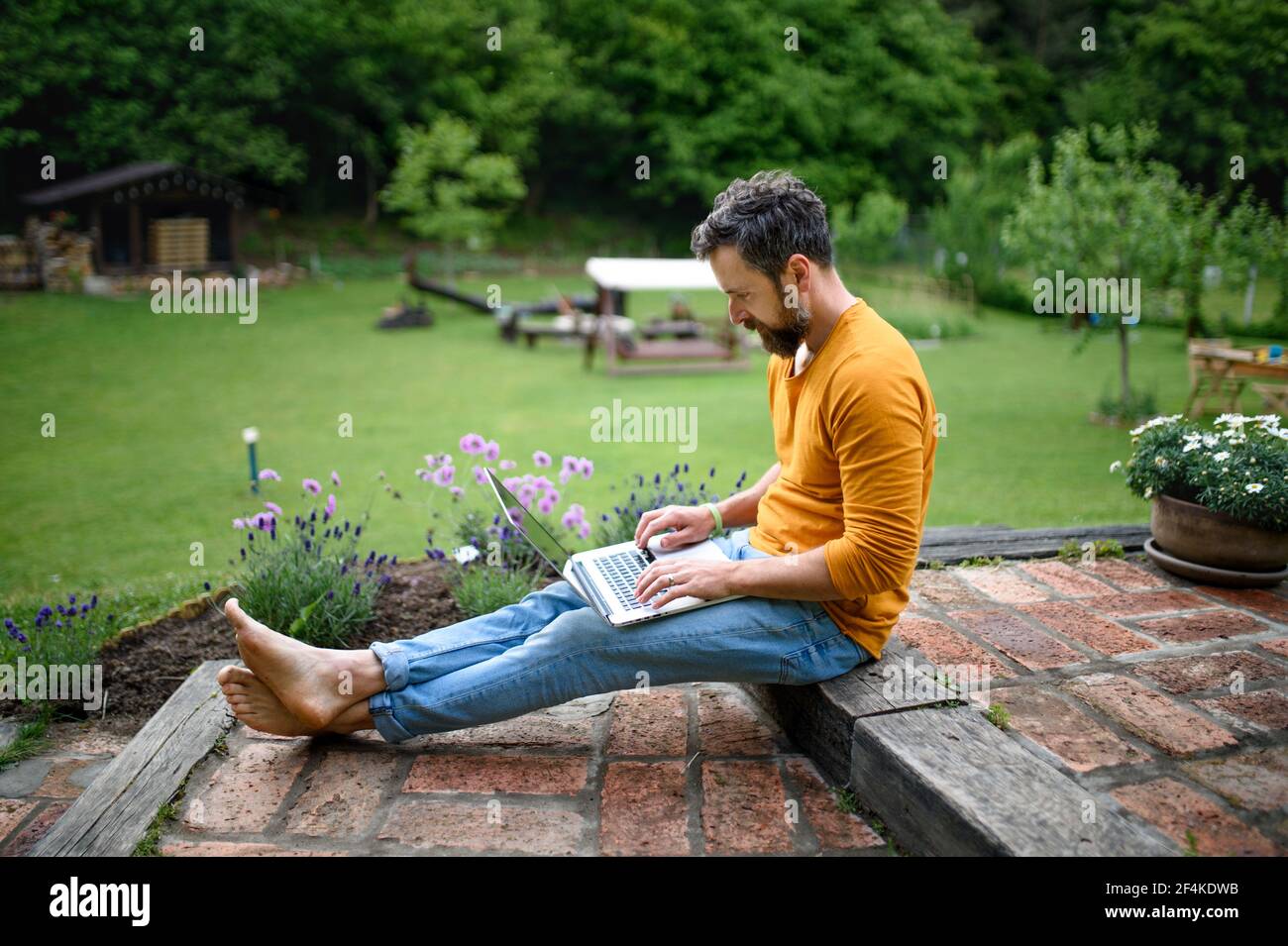 Reifer Mann mit Laptop im Garten arbeiten, Green Home Office Konzept. Stockfoto