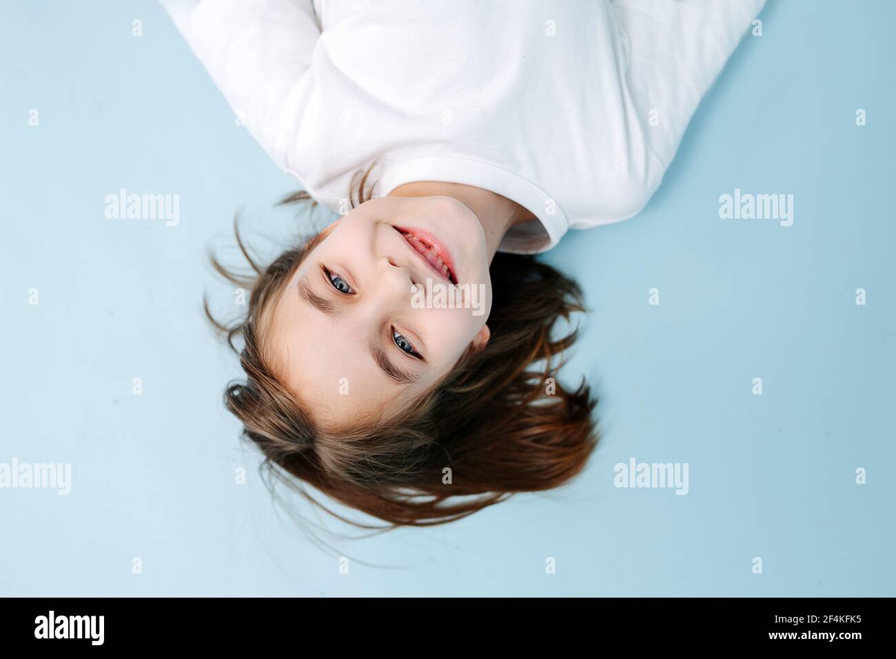 Draufsicht Porträt eines charmant lächelnden 9-jährigen Mädchen fehlt ein Zahn auf blauem Hintergrund. Studioaufnahme. Sie trägt blaue Jeans und weißes Hemd. Stockfoto