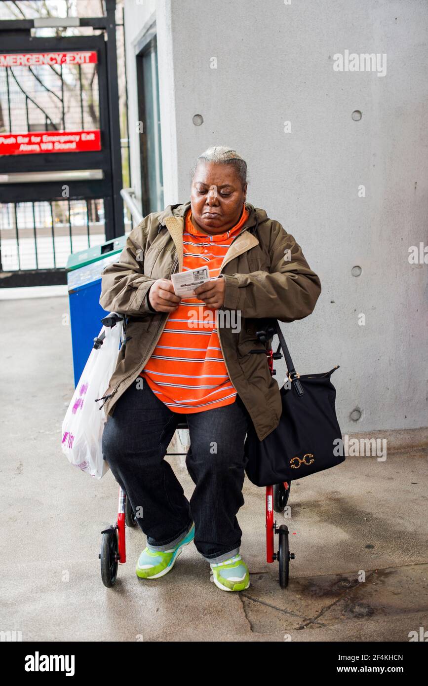 New York City, USA. Ältere Erwachsene afroamerikanische Frau, die auf ihrem Spaziergänger sitzt und auf die Roosevelt Island Tramway wartet, die sie über den East River führt. Stockfoto