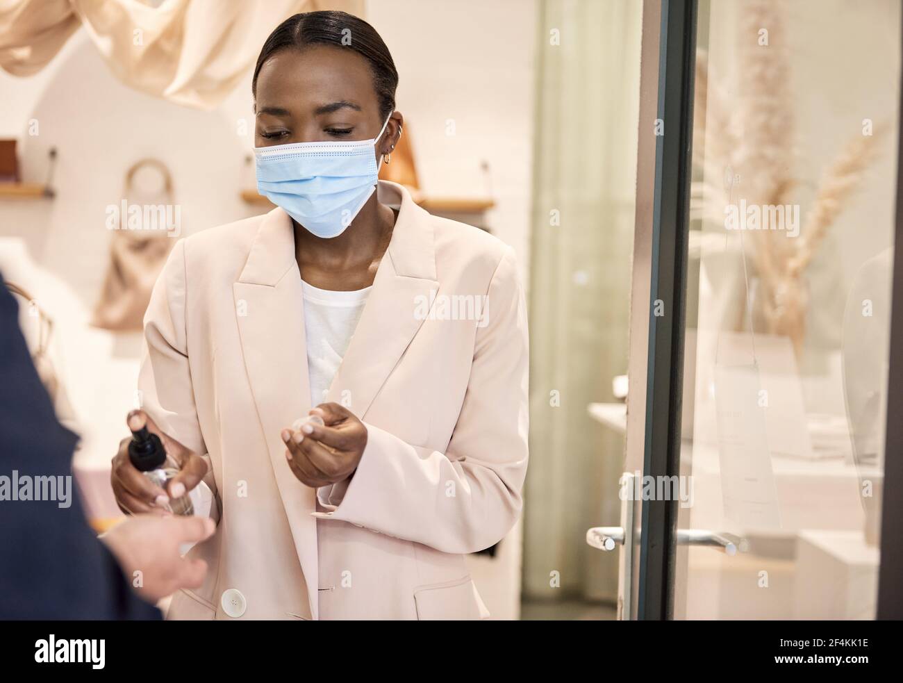 Afroamerikanische Ladenbesitzerin, die Desinfektionsmittel auf die eines Kunden anwendet Hände Stockfoto
