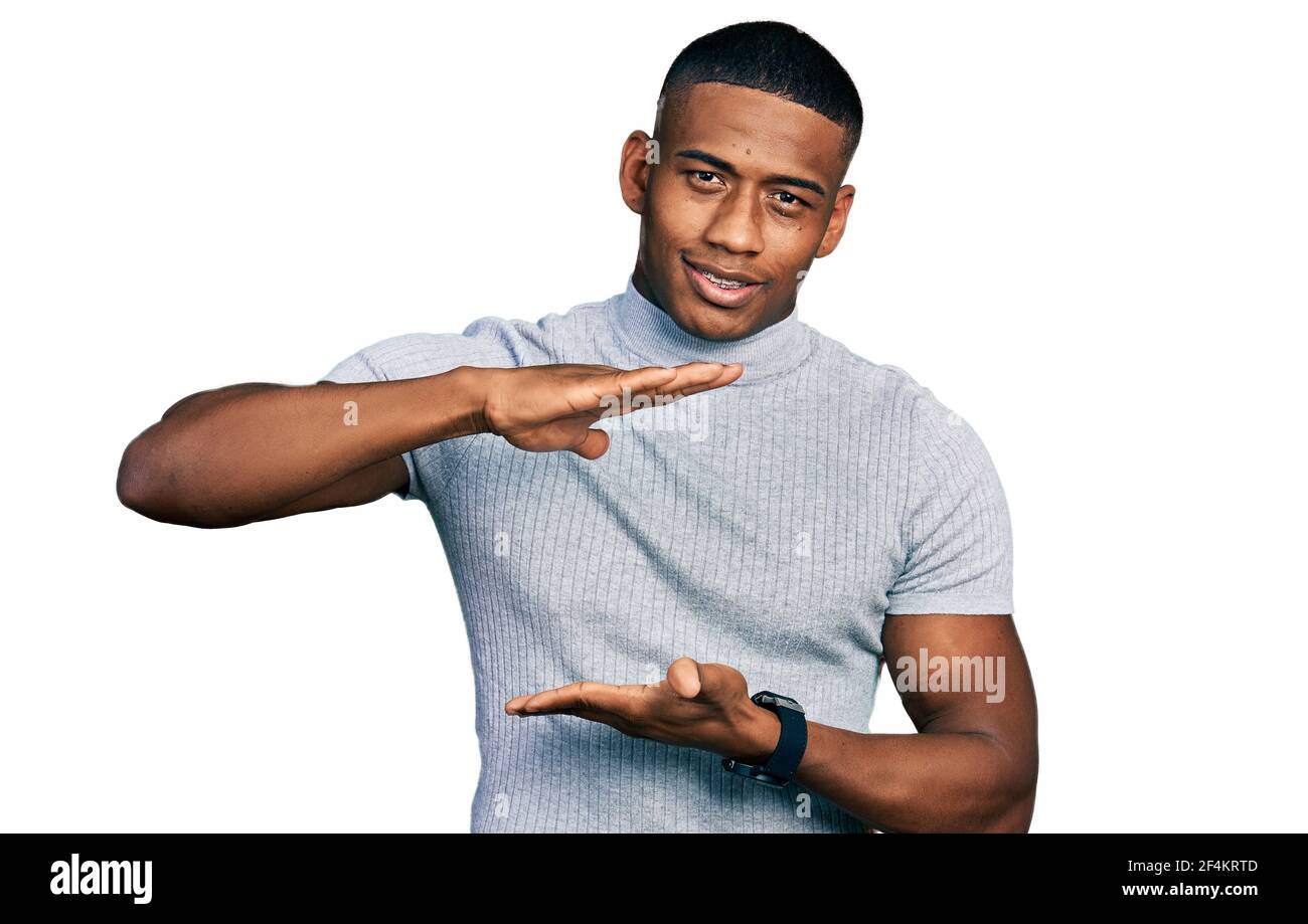 Junger schwarzer Mann trägt Casual T-Shirt gesturing mit Händen zeigt große und große Zeichen, Maßnahme Symbol. Lächelnd Blick auf die Kamera. Messen Stockfoto