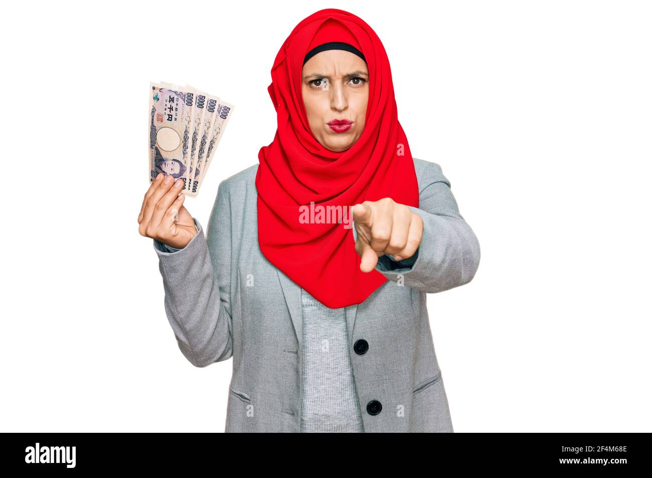 Schöne hispanische Frau trägt islamischen Hijab hält japanische Yen Banknoten zeigen mit dem Finger auf die Kamera und Sie, selbstbewusste Geste suchen Stockfoto