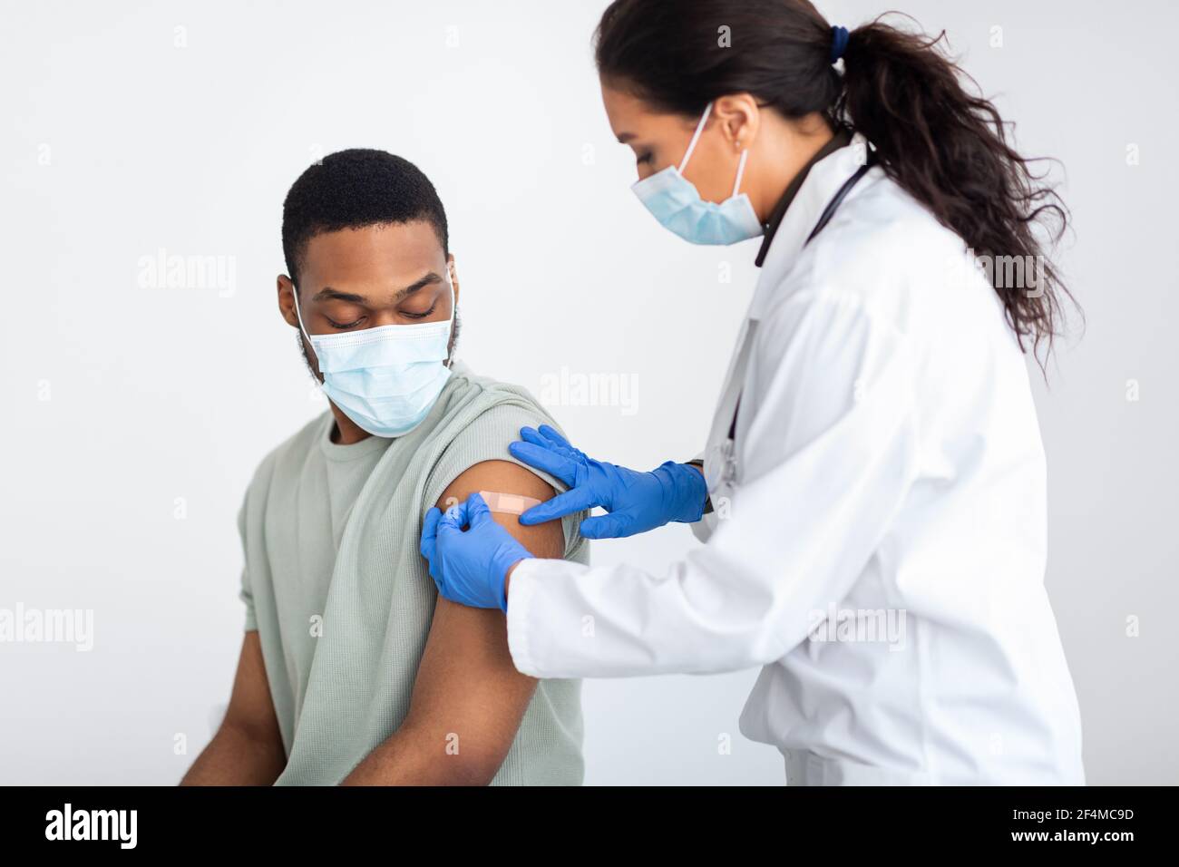 Arzt, der Gips auf den Arm des Mannes nach der Impfung anwendet, weißer Hintergrund Stockfoto