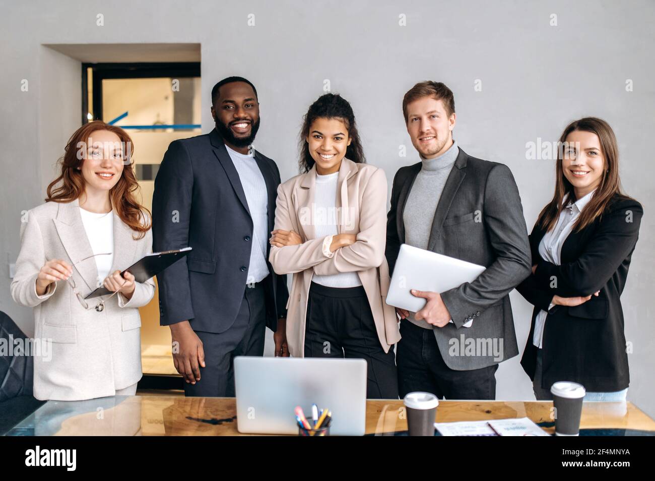 Porträt einflussreicher Geschäftsleute im modernen Büro. Erfolgreiche multiethnische Kollegen in stylischen Anzügen blicken direkt auf die Kamera, lächelnd, partnerschaftliches Konzept Stockfoto