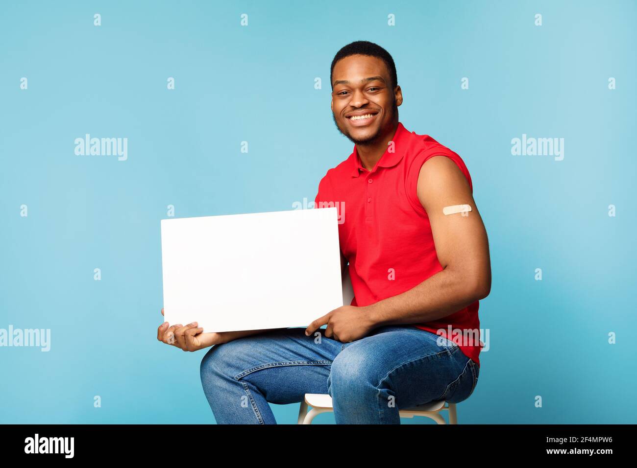 Geimpft Schwarz Guy Zeigt Blank Poster Sitzt Über Blauen Hintergrund Stockfoto