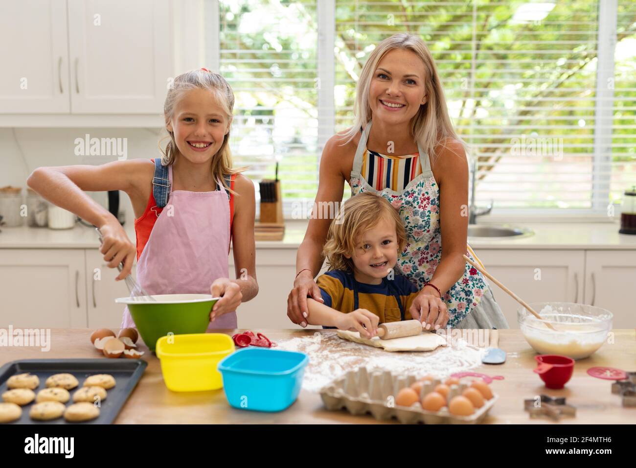 Lächelnde kaukasische Mutter, Tochter und Sohn tragen Schürzen und backen gemeinsam in der Küche Kekse Stockfoto