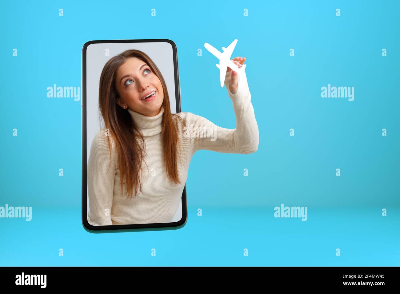 Reise, Urlaubskonzept. Ein Mädchen mit einem weißen Papierflugzeug guckt aus dem Smartphone-Bildschirm. Junge Frau ist online in einem Handy. Stockfoto