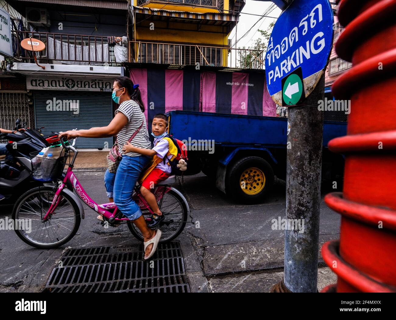 Eine Radfahrerin, mit einem jungen Schuljungen Beifahrer, fährt ihr Fahrrad entlang einer schmalen Soi in Talat Noi, Bangkok, Thailand Stockfoto