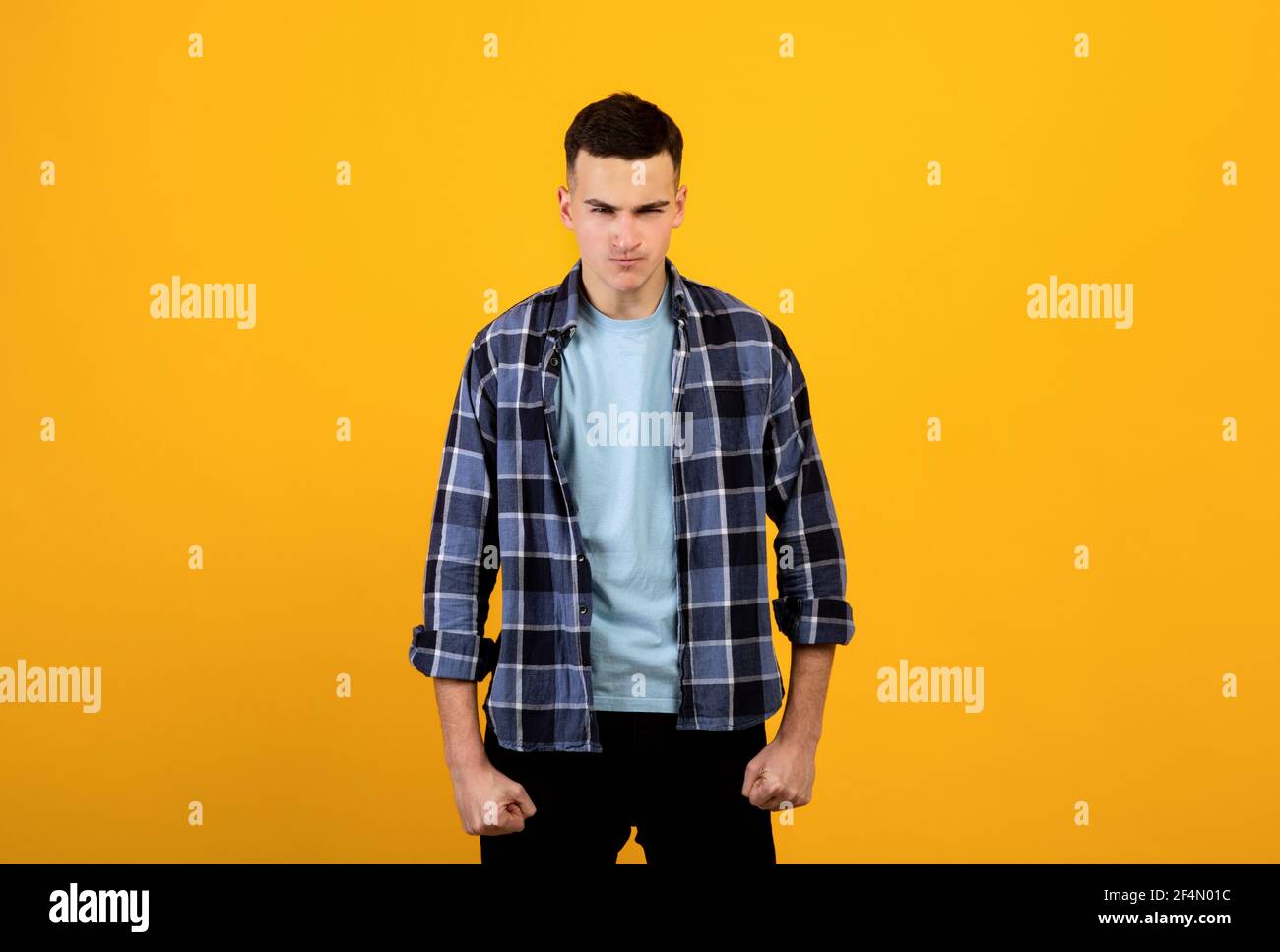 Erzürnte tausendjährige Mann, der seine Fäuste zusammenhält und versucht, seinen Zorn auf orangefarbenem Hintergrund zu unterdrücken. Negative Emotionen des Menschen Stockfoto