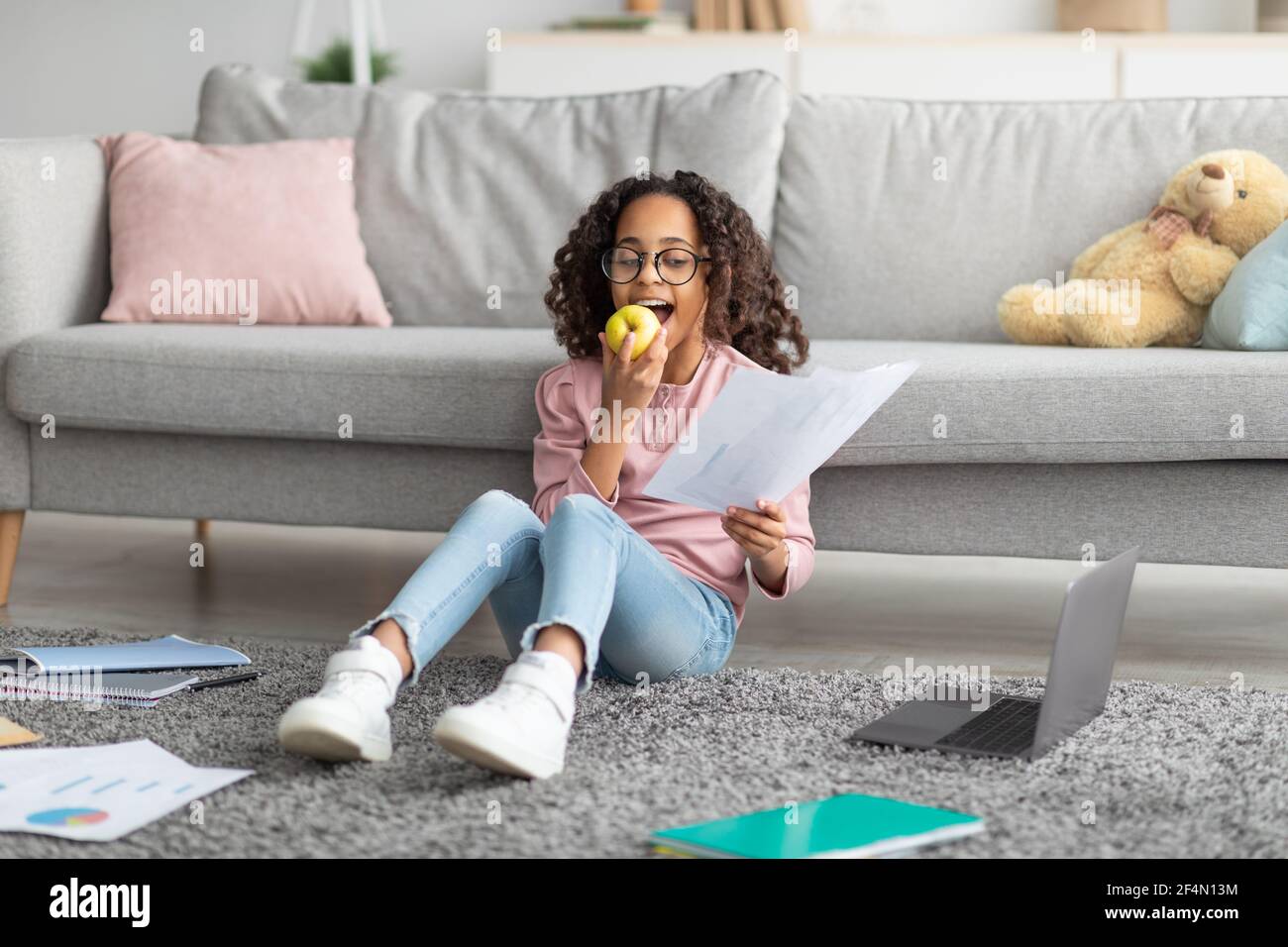 Smart afrikanisch-amerikanische Schülerin mit pädagogischen Materialien zu Hause studieren, Vorbereitung für Test und Apfel essen Stockfoto