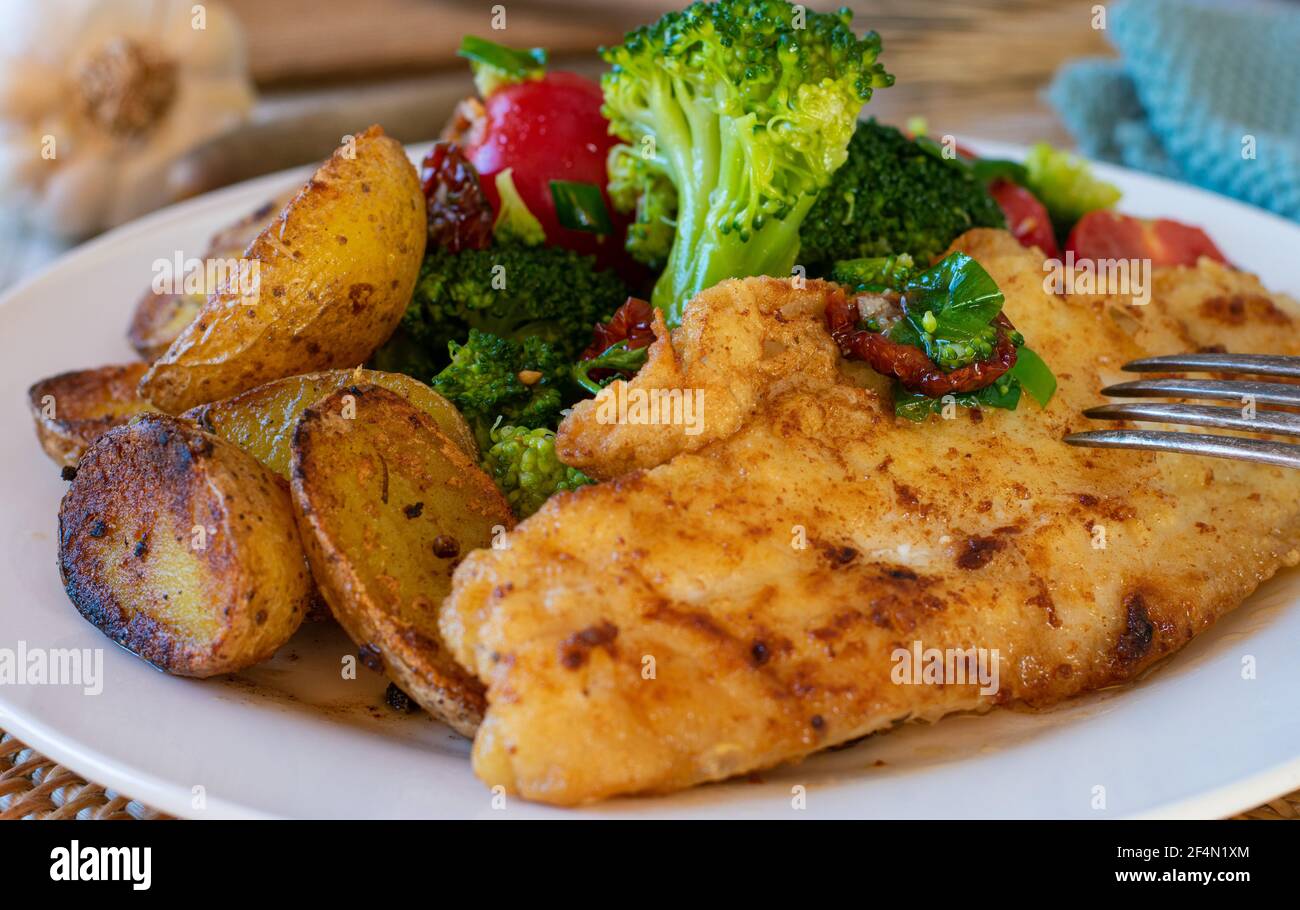 mediterranes Fischgericht mit gebratenem Rotbarsch-Filet, gerösteten Rosmarinkartoffeln und einem Brokkoli, Tomatensalat auf einem Teller serviert. Nahaufnahme und isoliert Stockfoto