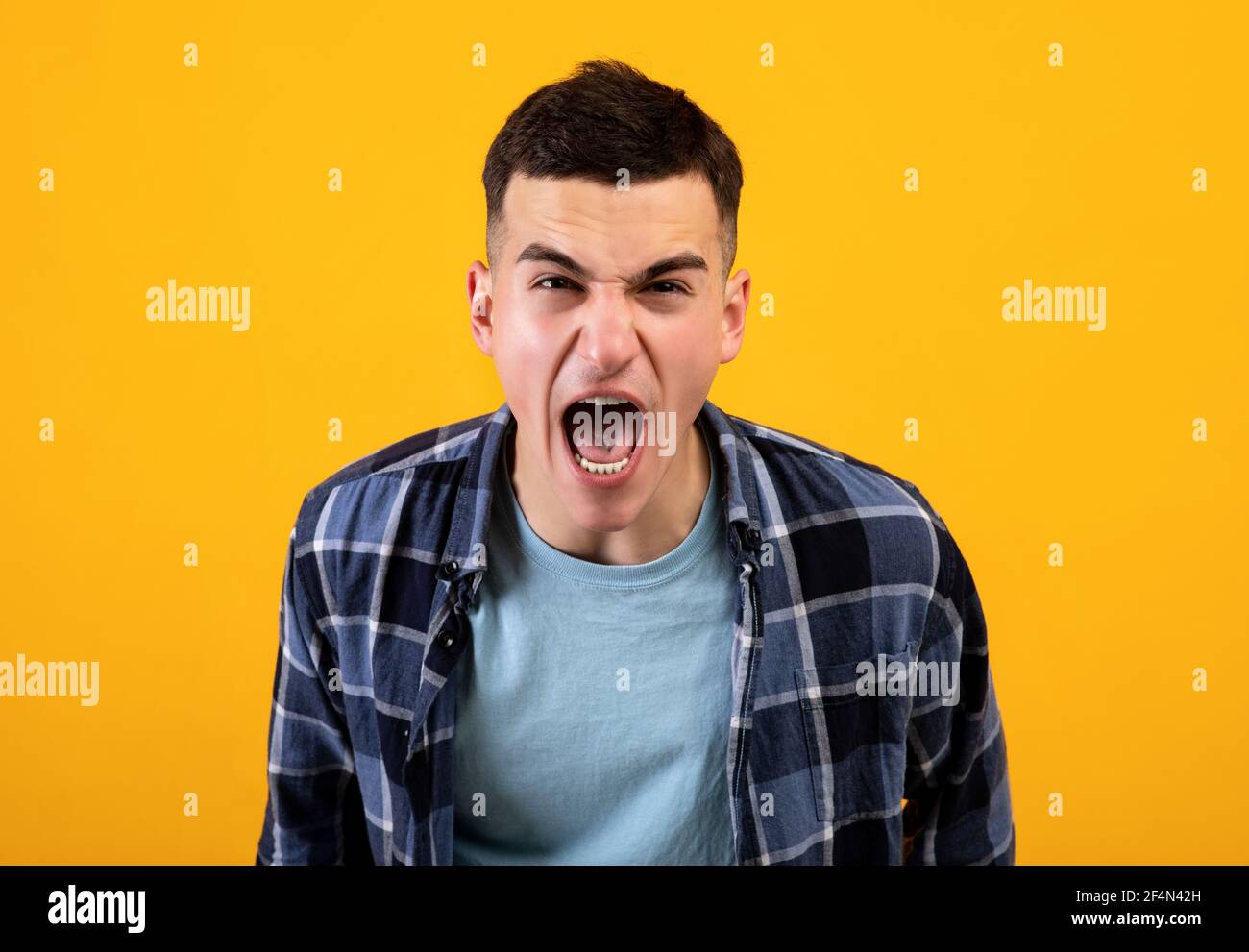 Frustrierter junger Mann, der vor Wut schreit und seine Wut über orangen Studiohintergrund ausdrückt. Konzept der negativen Emotionen Stockfoto