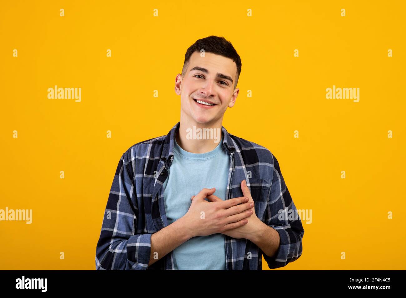 Aufrichtiger junger Kerl, der Hände auf sein Herz legt und Dankbarkeit auf orangefarbenem Studiohintergrund ausdrückt Stockfoto