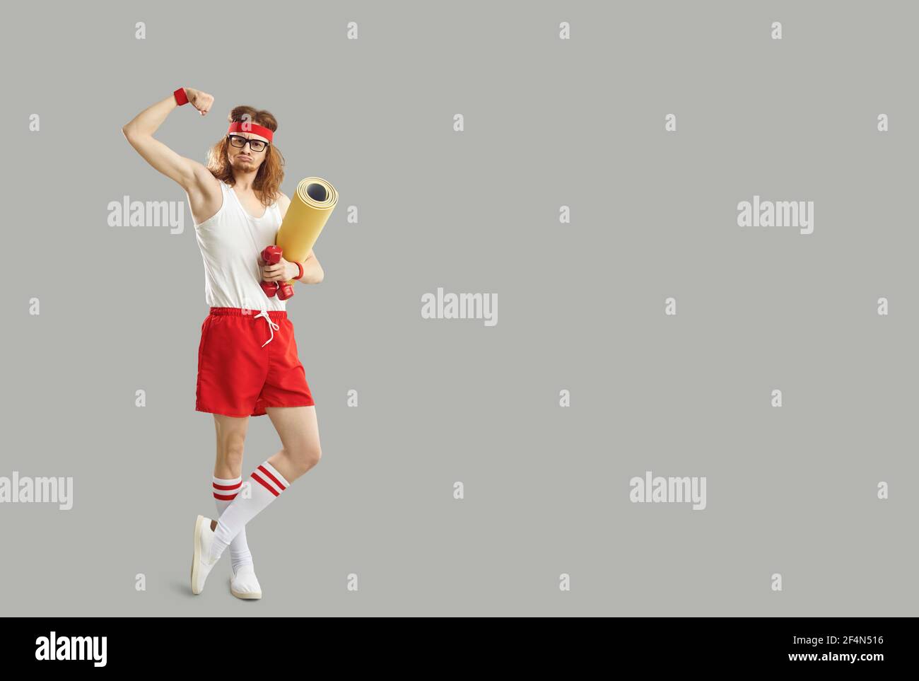 Lustige dünne Nerd hält seine Fitness-Matte und Hanteln und Zeigt seinen schwachen Bizep Stockfoto