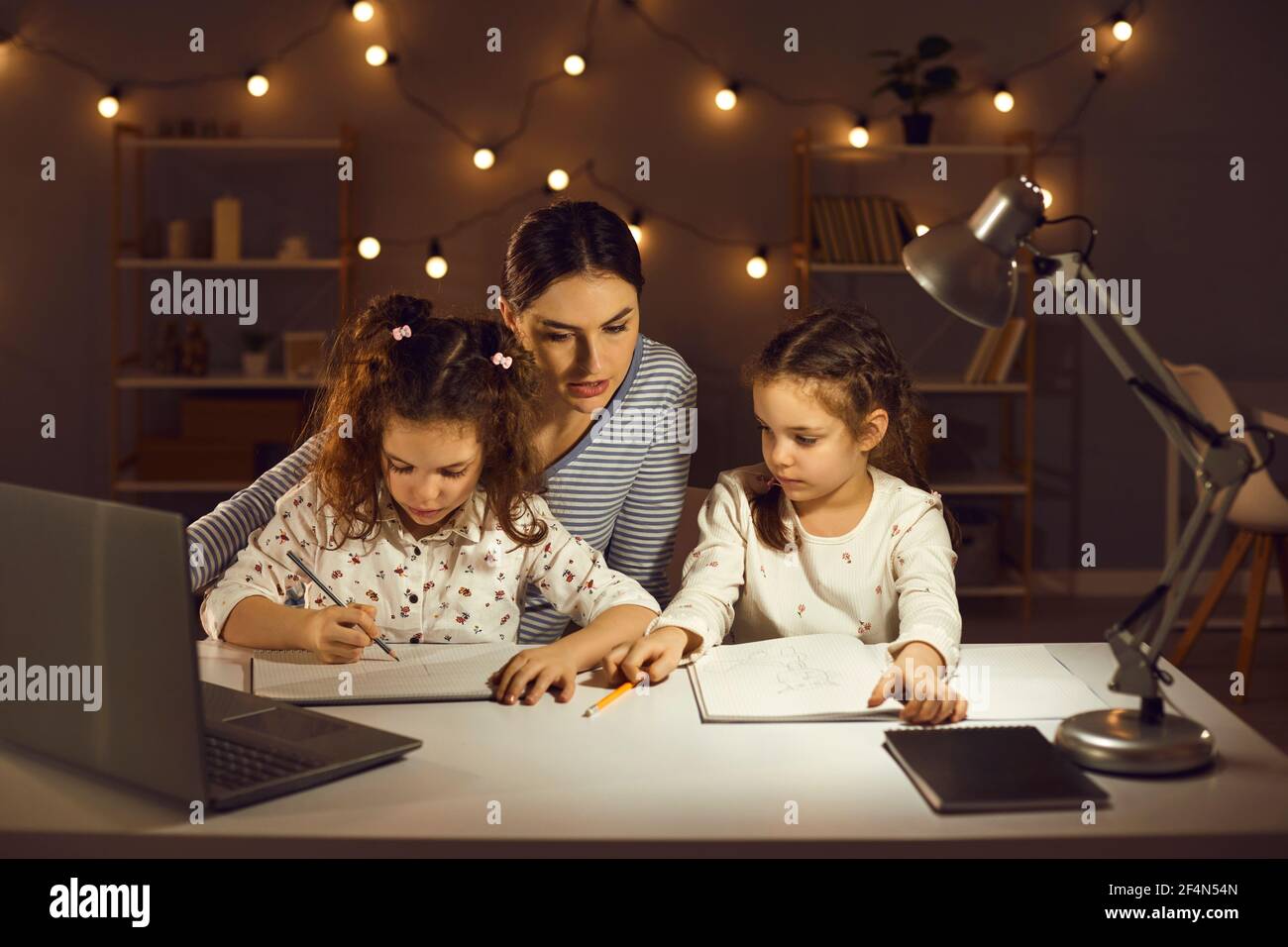 Mutter hilft kleinen Kindern, Schulaufgaben zu machen sitzen an Rezeption spät am Abend Stockfoto