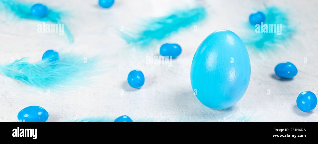 Banner mit blauem Ei auf weißem Beton-Hintergrund mit blauen Federn und blauen Pralinen in Form eines Eies. Frohe Ostern Konzept. Stockfoto