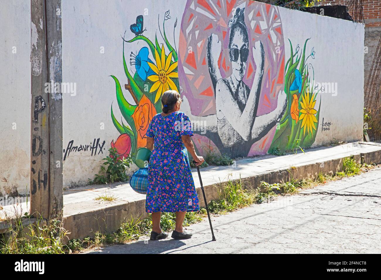 Ältere mexikanische Frau, die mit Gehstock an Graffiti Street Art an der Wand in der Stadt San Miguel de Allende, Guanajuato, Zentralmexiko vorbeigeht Stockfoto