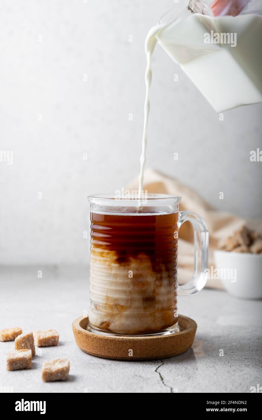 Kaltes Getränk mit Kaffee und Milch. Durchsichtiger Becher aus Glas, auf hellem Hintergrund. Vertikale Position Stockfoto