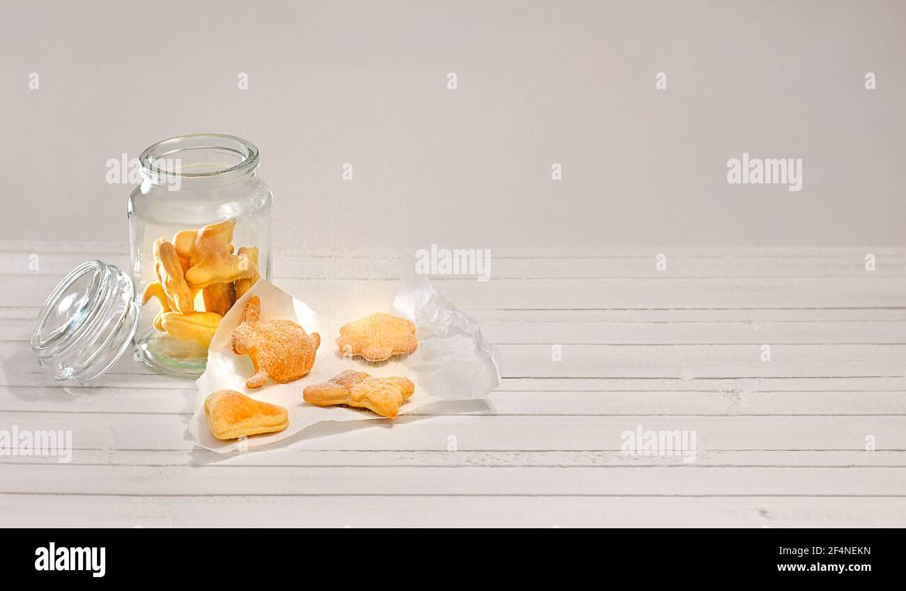 Glas mit lockigen Cookies bestreut mit Puderzucker. Auf einer weißen Holzarbeitsfläche. Stockfoto