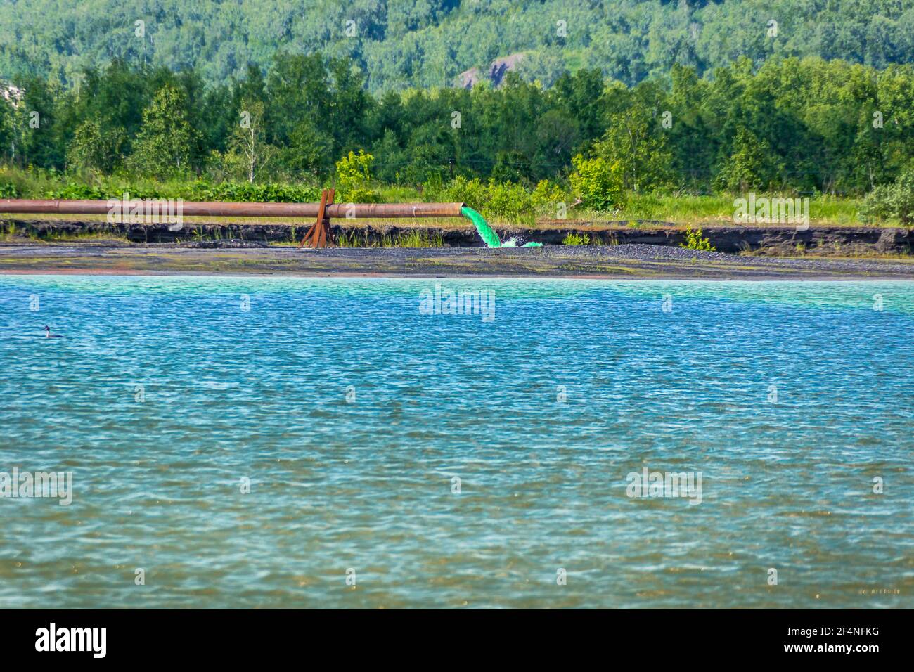 Aus einem rostigen Rohr werden flüssige Abfälle von giftiger grüner Farbe gegossen, die das Flusswasser verschmutzen und das aquatische Ökosystem zerstören Stockfoto