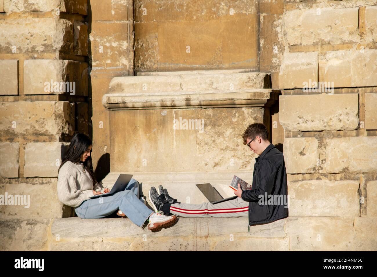 Oxford, UK 22 Nov 2020: Zwei Studenten sitzen in der Sonne auf Ratcliffe Kamerawand Hang mit Laptops zum Lernen. Junge Mädchen und Jungen Forschung informa Stockfoto