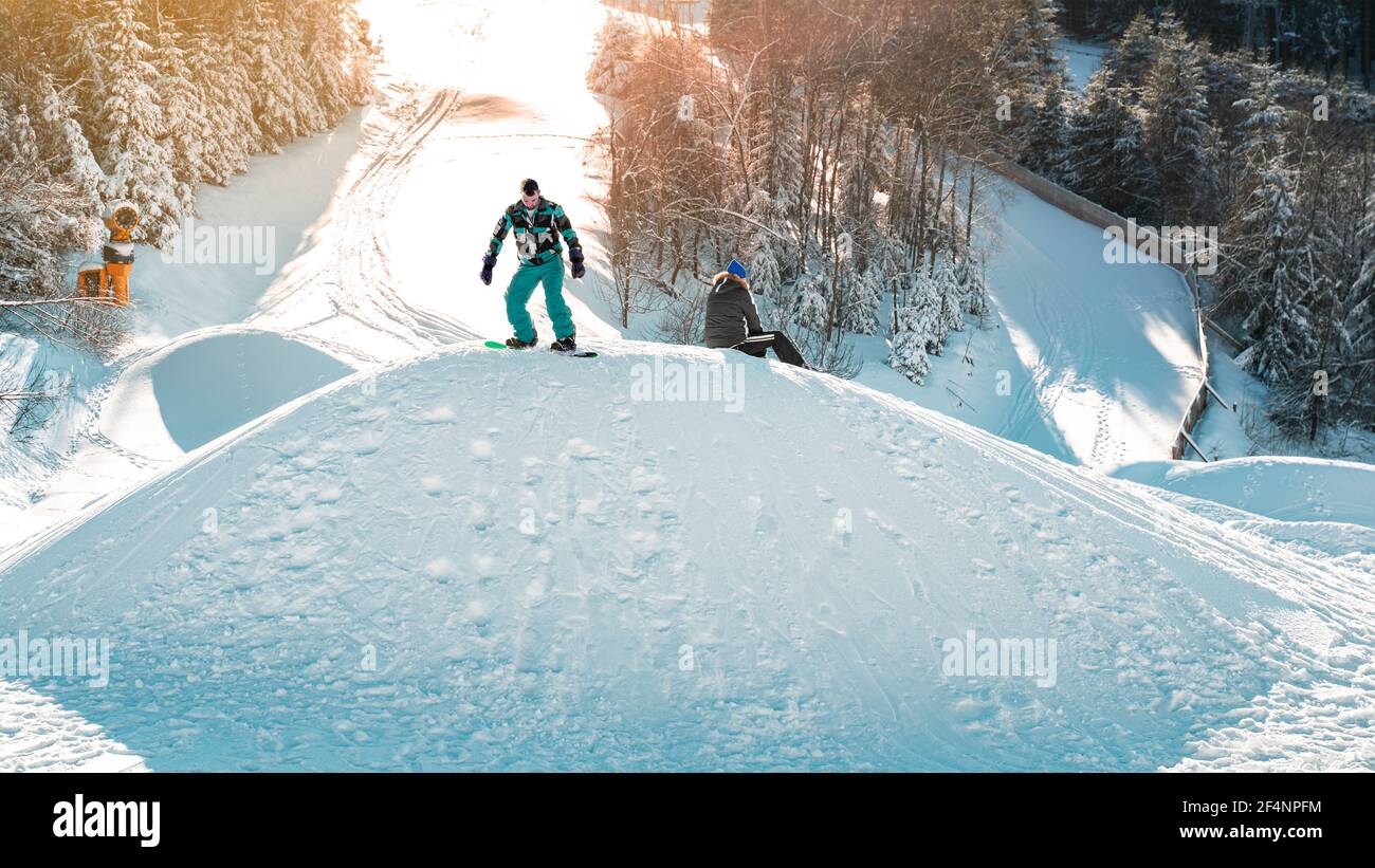 Wintersportgebiet mit Schnee und Sonnenschein. Ein Mann, der Snowboardcross  auf einem Schneehügel übt. Sein Freund ist Rodeln die Schanze hinunter.  Winterberg, Deutsch Stockfotografie - Alamy