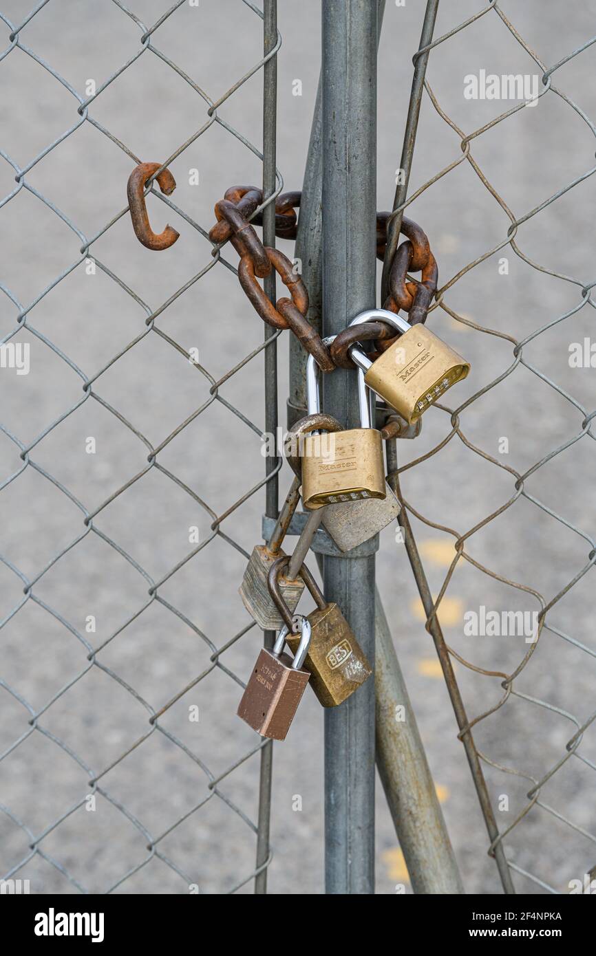 Mehrere Vorhängeschlösser mit einer dicken rostigen Kette am Drahtzaun Zutritt zum dahinter liegenden Grundstück ist verboten Stockfoto