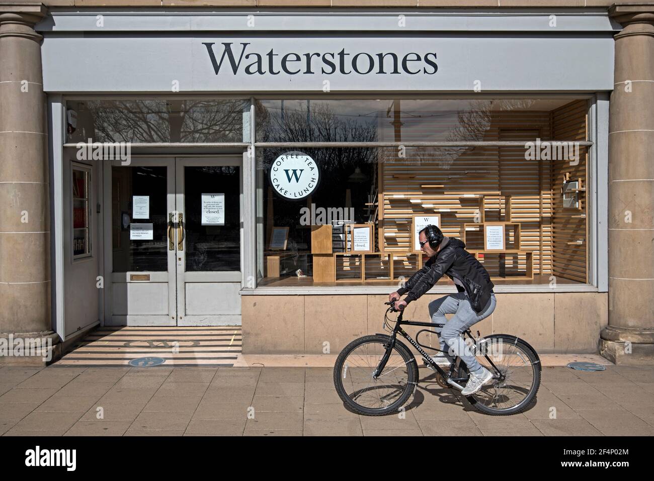Der junge Mann, der während der zweiten covid Lockdown an einer Abzweigung der Waterstoneson Princes Street, Edinburgh Schottland, Großbritannien, vorbei radelt. Stockfoto