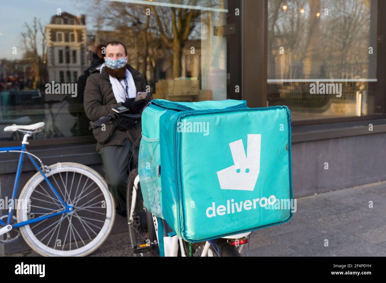 Deliveroo Biker wartet vor dem Restaurant auf seine Bestellung neben seinem Fahrrad mit Rucksack ausgestattet, London, England Stockfoto