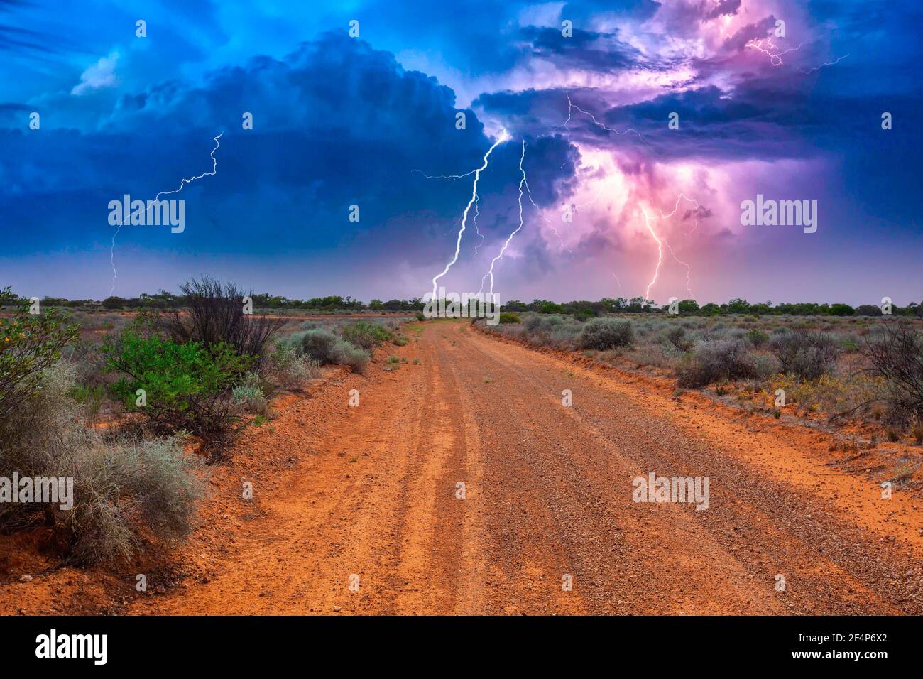 Verlassene australische Outback-Landschaft mit roter Schotterstraße zum Horizont Mit Büschen an Straßenrändern und schwerem Gewitter mit weißem Purpur Blitze Stockfoto